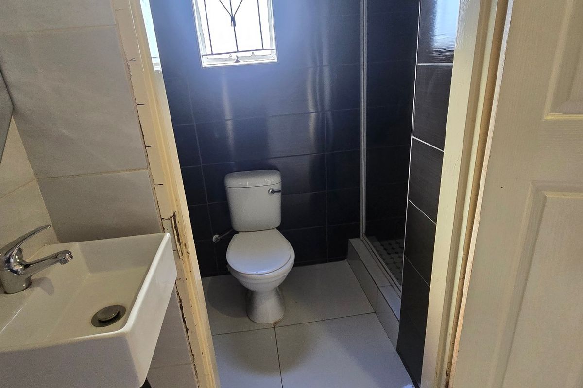 Compact bathroom featuring a wall-mounted basin, toilet, and a shower enclosure with dark tiled walls and light floor tiles.