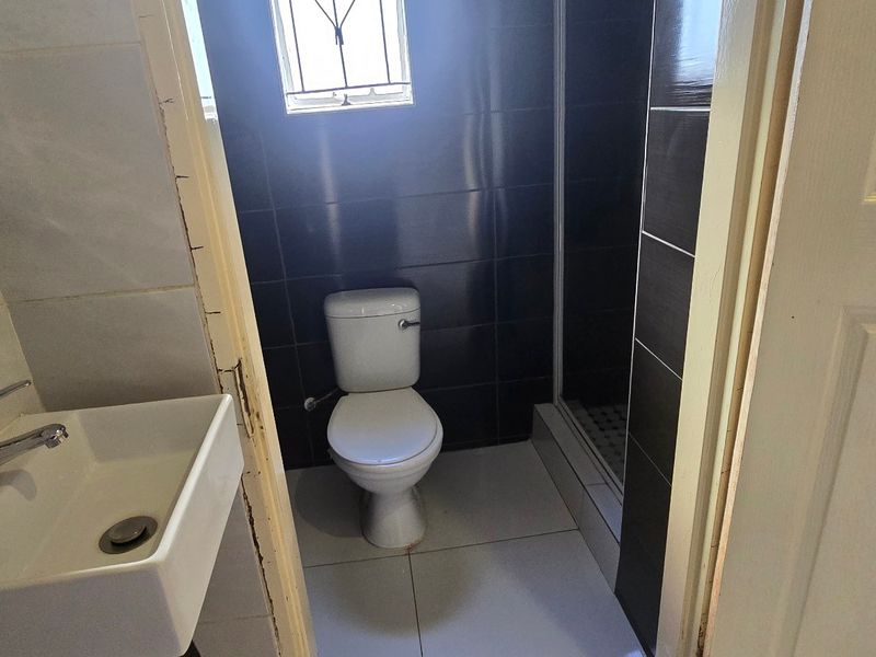 Compact bathroom featuring a wall-mounted basin, toilet, and a shower enclosure with dark tiled walls and light floor tiles.