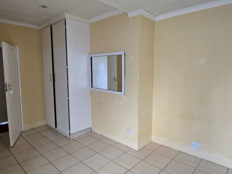 An empty bedroom featuring tiled flooring, a built-in wardrobe, and neutral wall finishes, offering a blank canvas for potential updates and personalization.