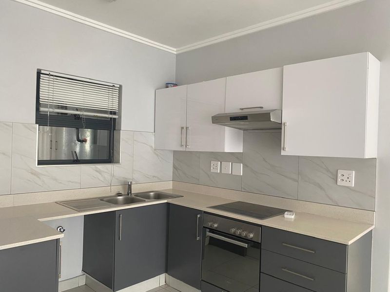 Modern kitchen featuring two-tone cabinetry, stone countertops, marble-look tile backsplash, and integrated stainless steel appliances including an oven, hob, and extractor fan.
