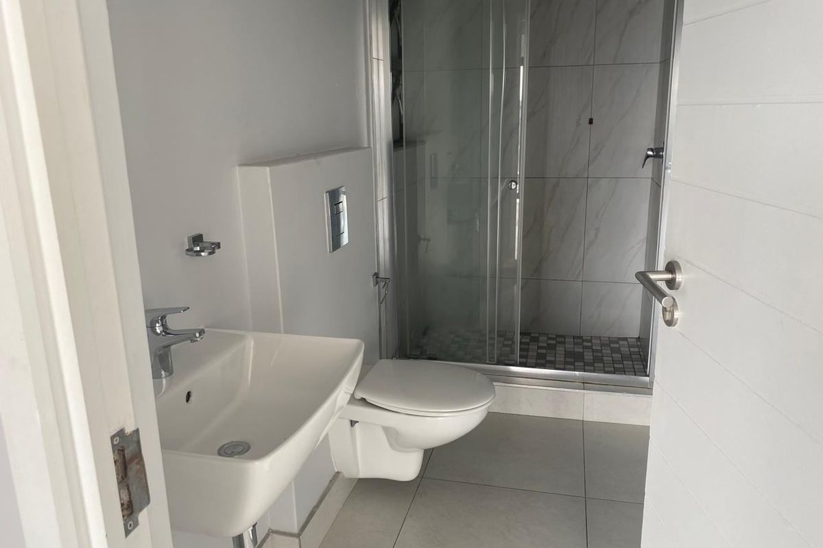 A clean, modern bathroom featuring a wall-mounted toilet, a basin with a chrome mixer tap, and a glass-enclosed shower with tiled finishes.
