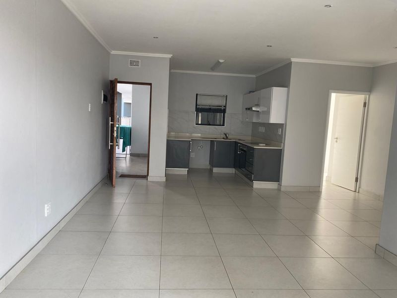 Spacious open-plan living area featuring neutral tiled flooring, recessed lighting, and a modern kitchen with built-in cabinetry and integrated appliances.