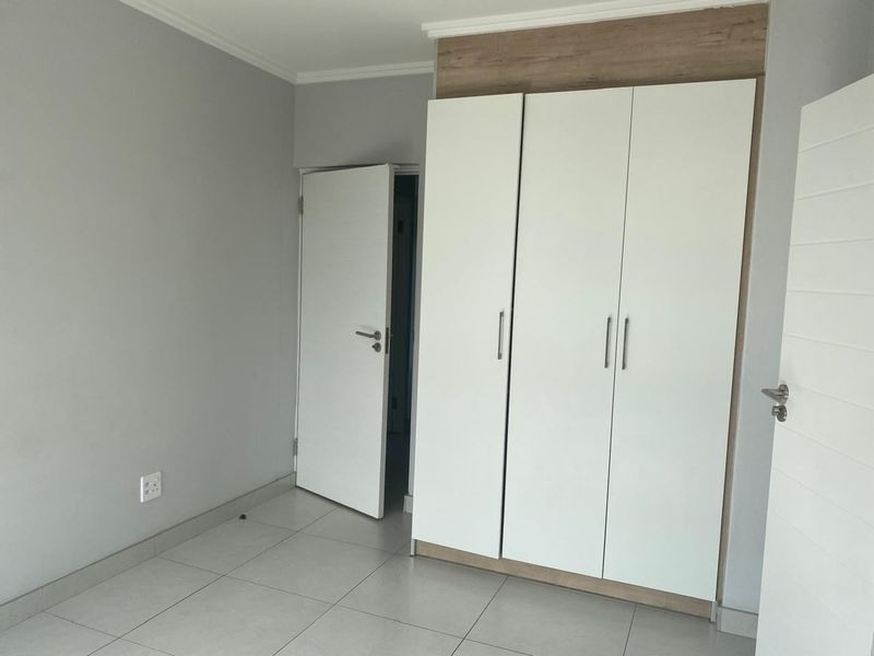 A clean, empty bedroom featuring modern built-in cupboards with wood-look accents and neutral tiled flooring.