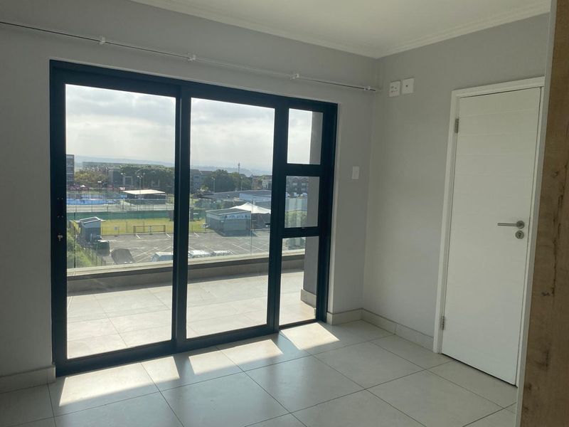 A bright, empty living area featuring large sliding glass doors that open onto a balcony, with neutral tiled flooring and clean finishes.