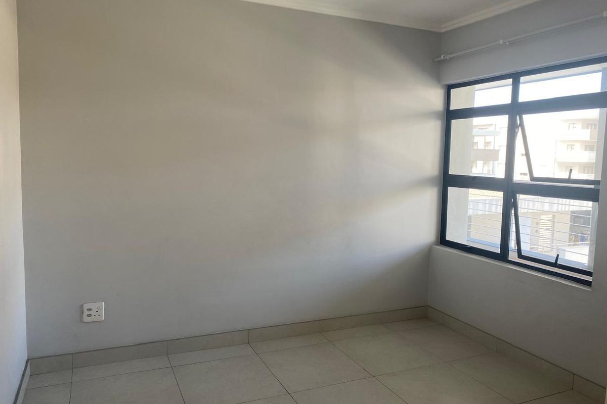 An empty bedroom featuring neutral tiled flooring, clean walls, and a large aluminium-framed window providing natural light.