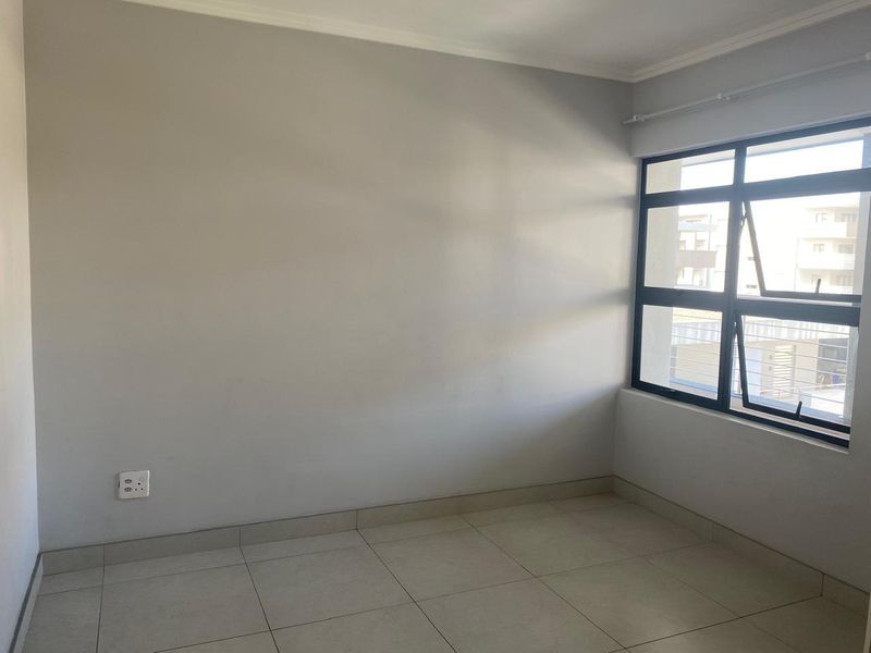 An empty bedroom featuring neutral tiled flooring, clean walls, and a large aluminium-framed window providing natural light.