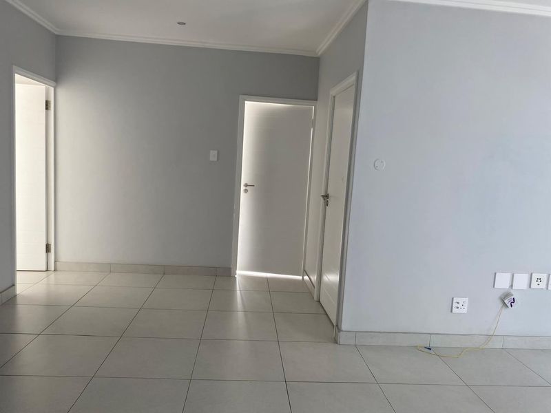 A bright, empty hallway featuring neutral grey walls, tiled flooring, and multiple internal doors, providing a clean and versatile transition space.