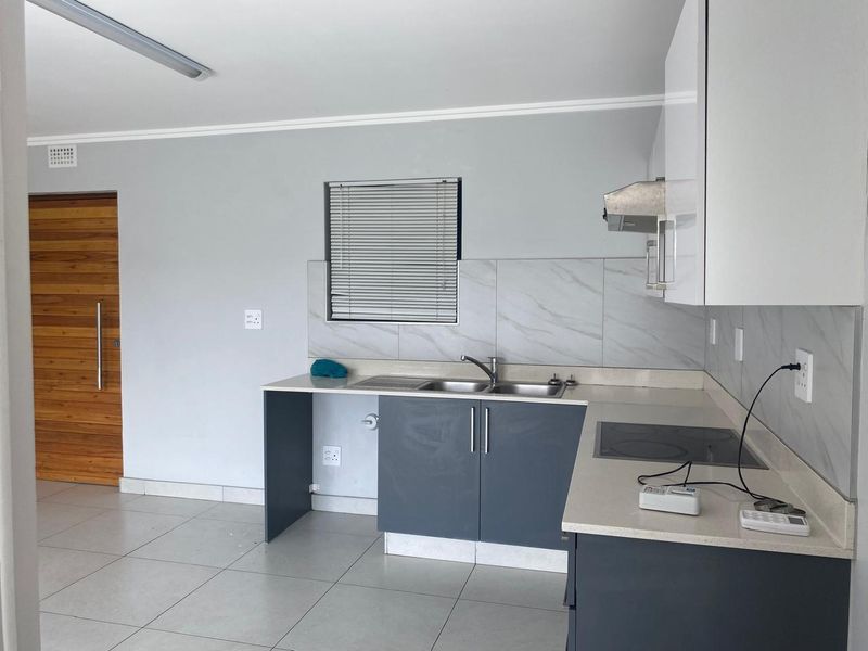 Modern kitchen featuring sleek grey cabinetry, stone countertops, integrated electric hob, extractor fan, and marble-look tiled backsplash in a clean, open-plan layout.