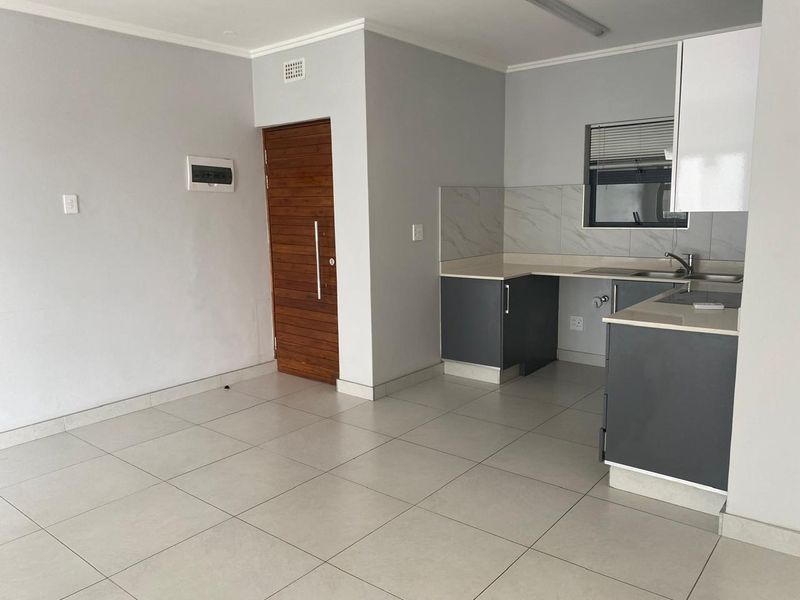 Modern open-plan living area featuring neutral tiled flooring, a contemporary kitchen with stone countertops, and a secure timber entrance door.