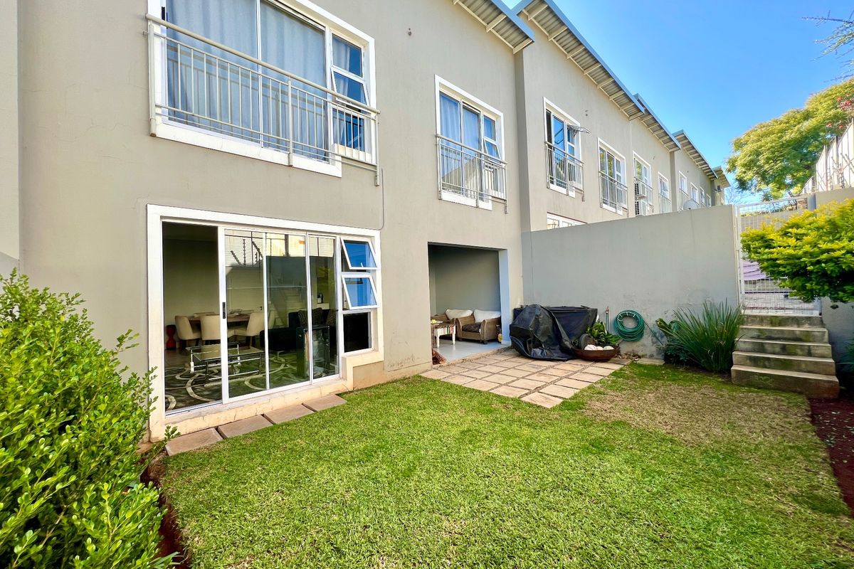 Rear view of the cluster property featuring a private garden, paved patio area, and upper-level balconies with sliding door access to the living space.