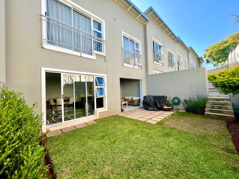 Rear view of the cluster property featuring a private garden, paved patio area, and upper-level balconies with sliding door access to the living space.