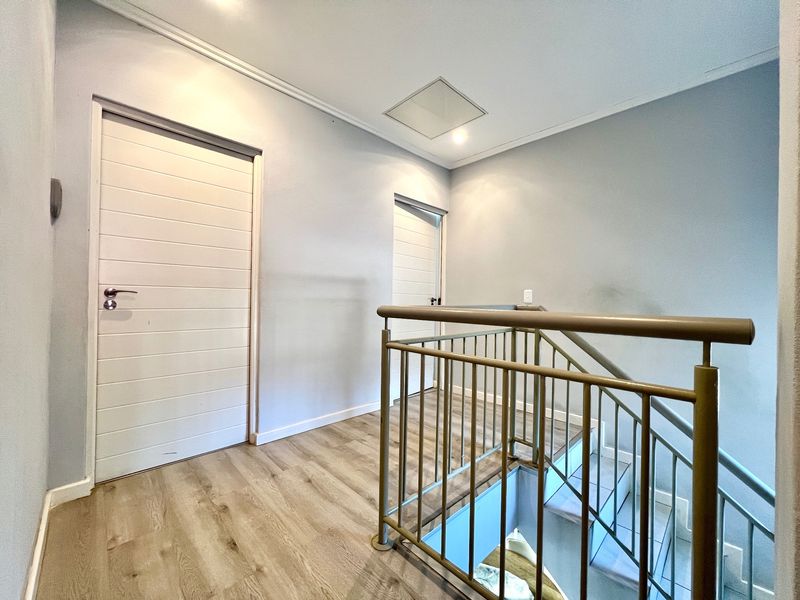 A bright upper-level landing area featuring laminate flooring, a metal staircase railing, and access to multiple internal rooms.