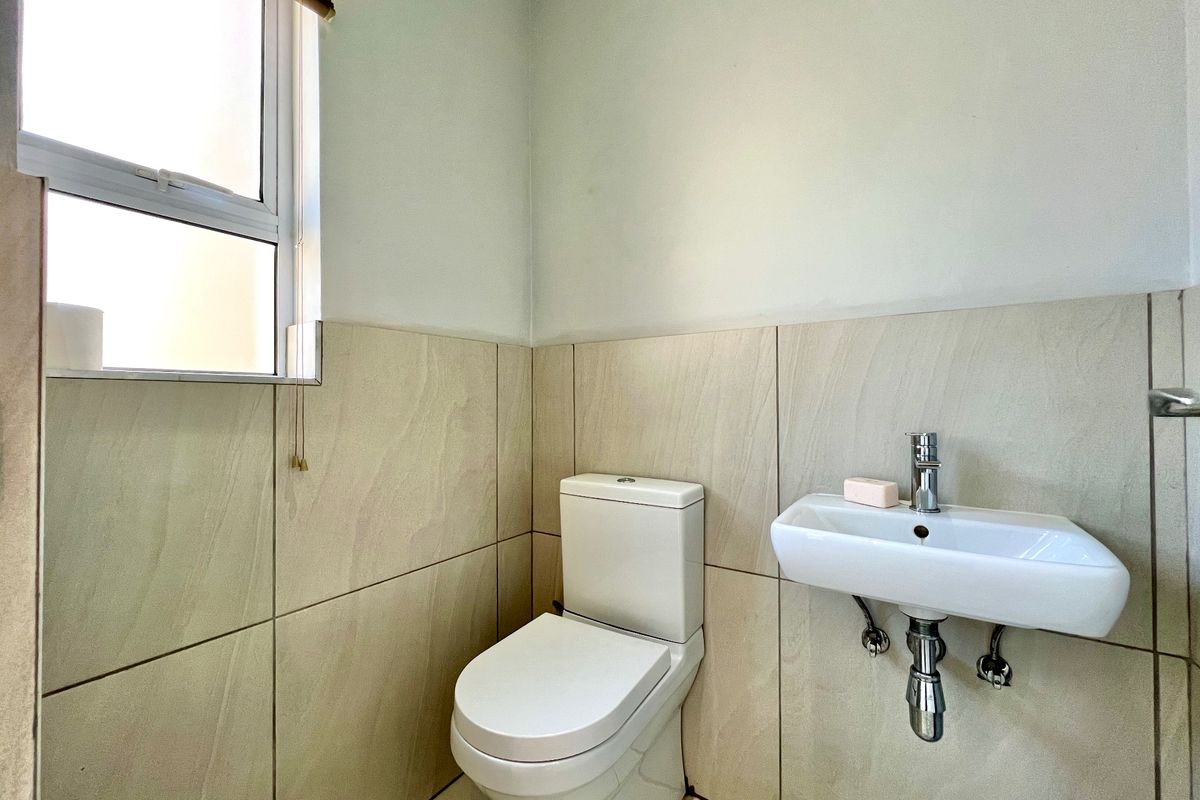 A compact guest bathroom featuring a wall-mounted basin, chrome mixer tap, and a modern toilet with neutral wall tiling.