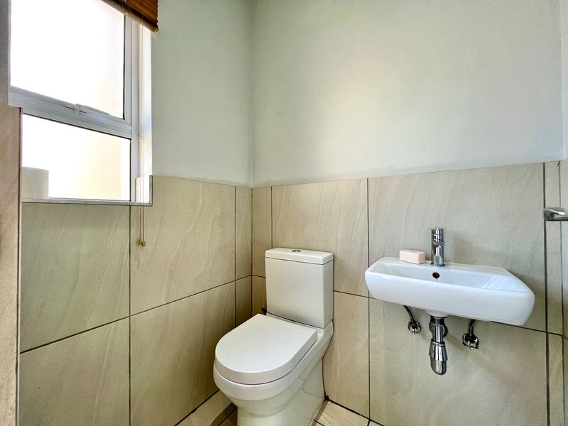 A compact guest bathroom featuring a wall-mounted basin, chrome mixer tap, and a modern toilet with neutral wall tiling.