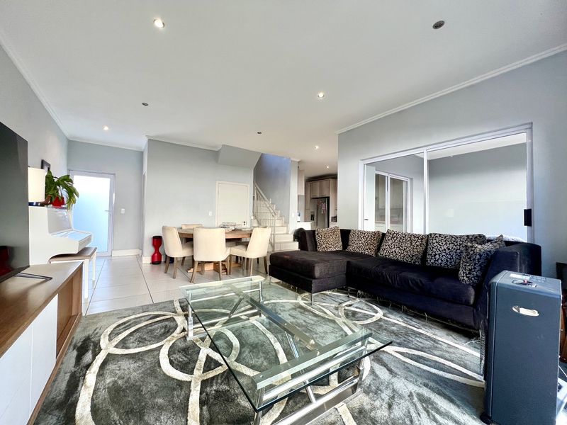 Spacious open-plan living and dining area featuring tiled floors, recessed lighting, and a staircase, with seamless flow to the adjacent kitchen and outdoor space.