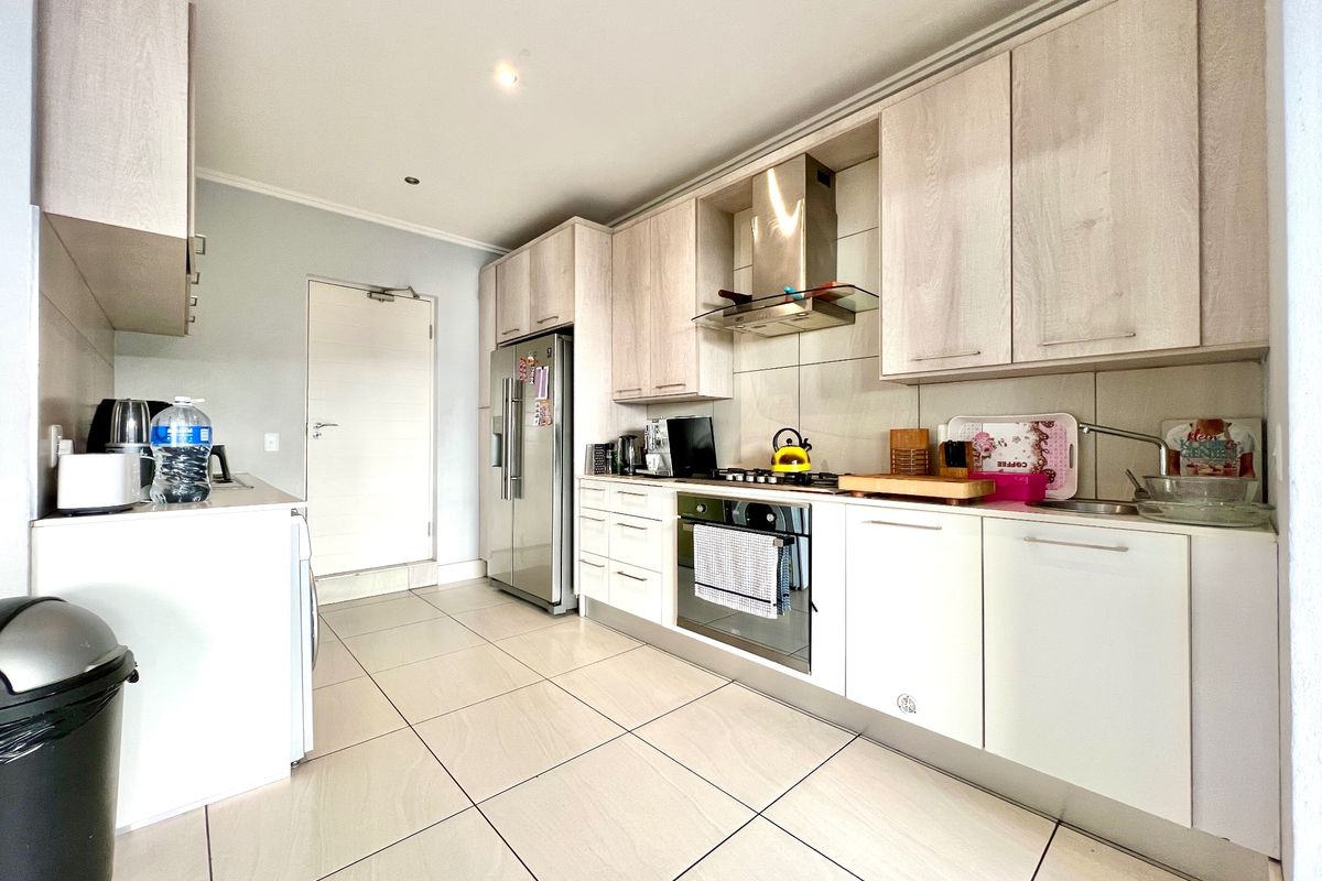 Modern kitchen featuring light wood-finish cabinetry, stainless steel appliances, gas hob, extractor fan, and neutral tiled flooring.