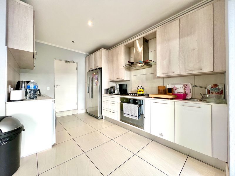 Modern kitchen featuring light wood-finish cabinetry, stainless steel appliances, gas hob, extractor fan, and neutral tiled flooring.