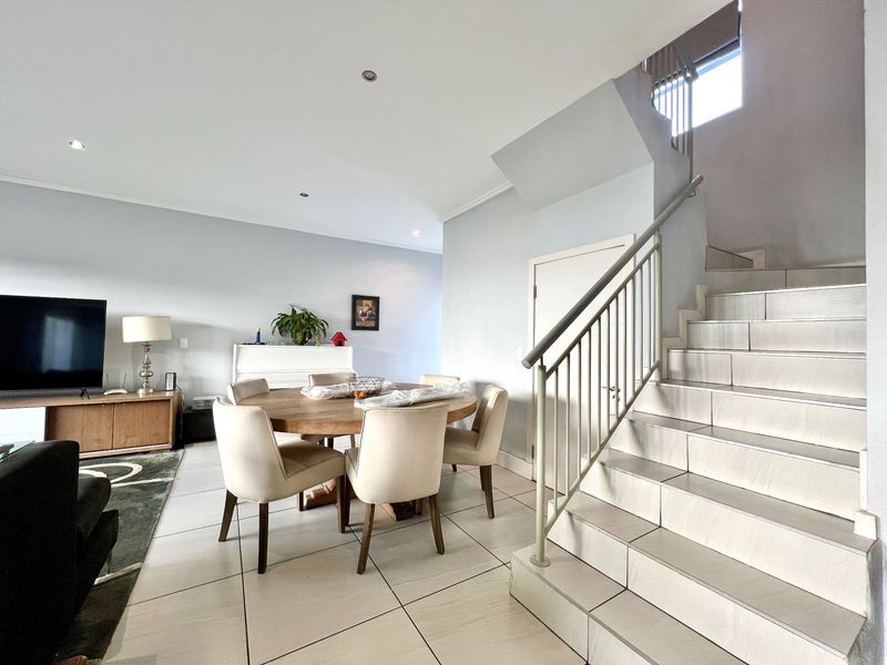 Open-plan living and dining area featuring tiled flooring, recessed lighting, and a staircase with a metal balustrade leading to the upper level.