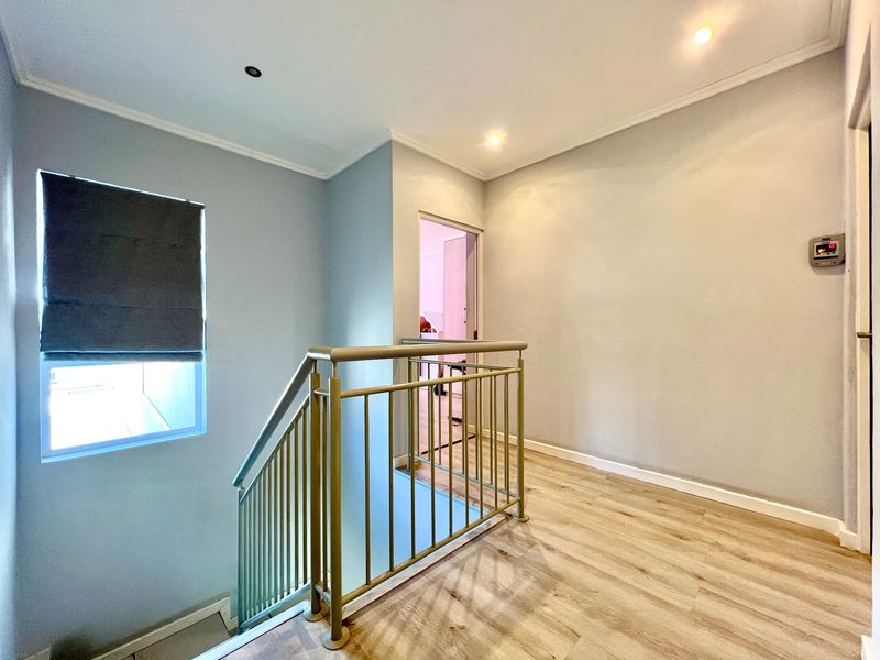 A bright, empty upper-level landing area featuring modern laminate flooring, a metal balustrade, and recessed ceiling lighting.