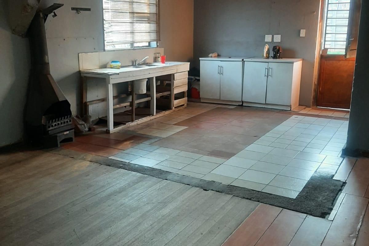 An open-plan kitchen area featuring a mix of wooden and tiled flooring, a built-in fireplace, and basic cabinetry, requiring significant renovation and modernization.