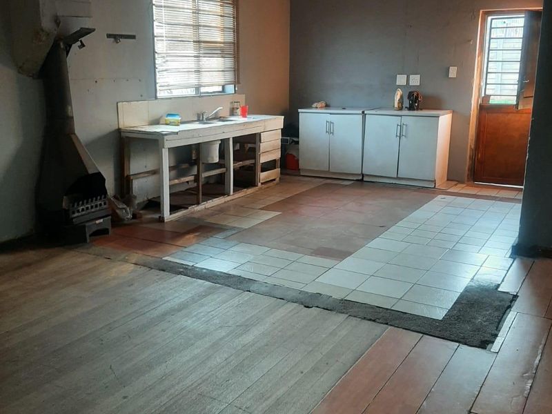 An open-plan kitchen area featuring a mix of wooden and tiled flooring, a built-in fireplace, and basic cabinetry, requiring significant renovation and modernization.