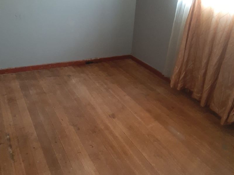 An empty bedroom featuring original timber flooring and neutral wall paint, offering a blank canvas for renovation or interior design updates.