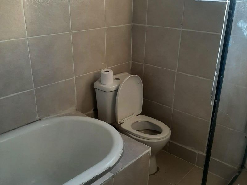 A functional bathroom featuring a built-in bathtub, toilet, and shower enclosure with tiled finishes, requiring some cosmetic attention to the bathtub edge and wall paint.