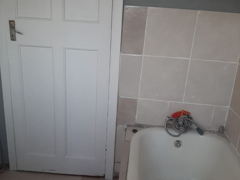 A compact bathroom featuring a built-in bathtub with a handheld shower mixer and neutral wall tiling.