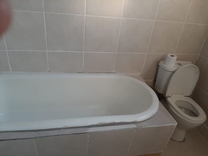 A functional bathroom featuring a standard bathtub with tiled surround and a toilet, requiring cosmetic updates to finishes and grout.