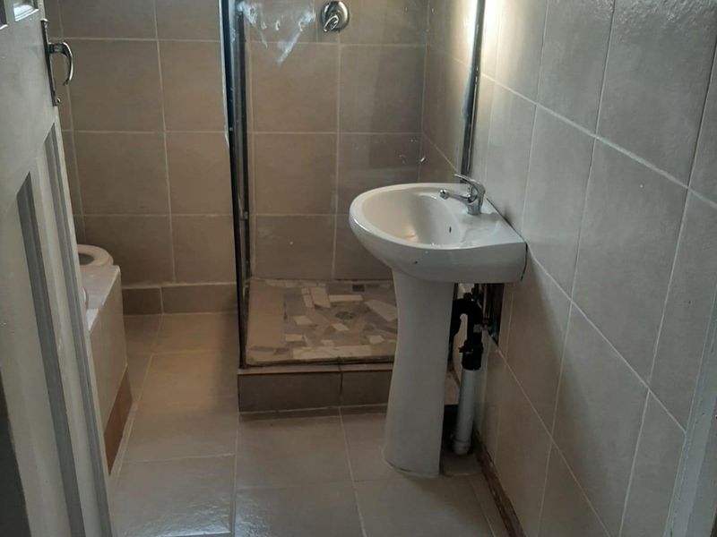 A compact bathroom featuring a pedestal basin, shower enclosure, and tiled finishes, currently requiring minor finishing work to the plumbing and wall edges.