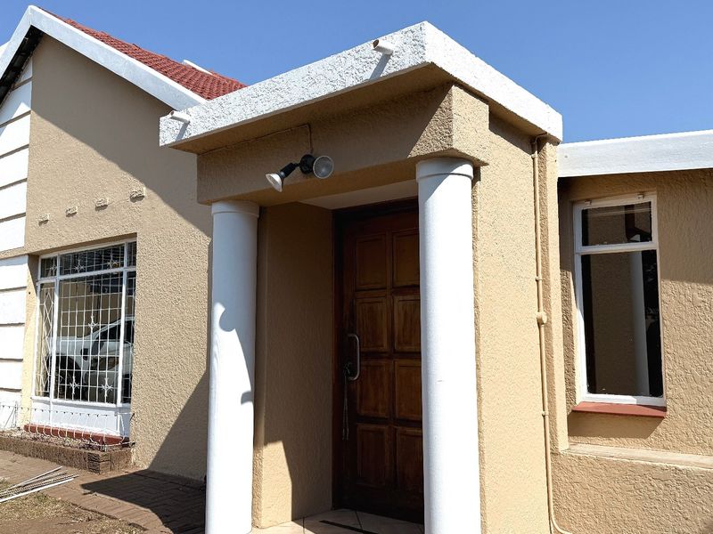 Front entrance of a house featuring a textured facade, decorative columns, and a solid wooden door with security-barred windows.