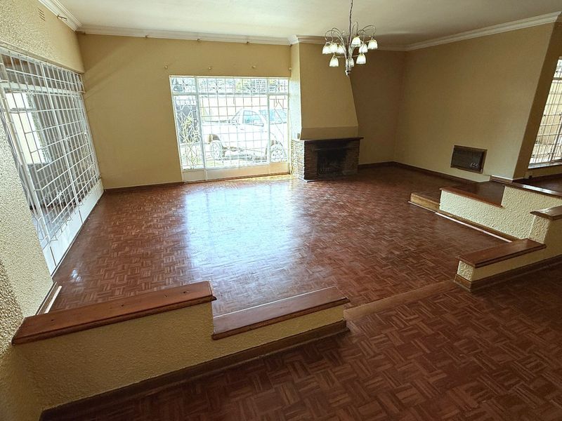 Spacious sunken living room featuring original parquet flooring, a built-in fireplace, and large windows with security bars.