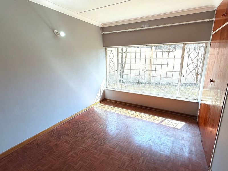 An empty bedroom featuring parquet flooring, a built-in cupboard, and large windows fitted with security bars.