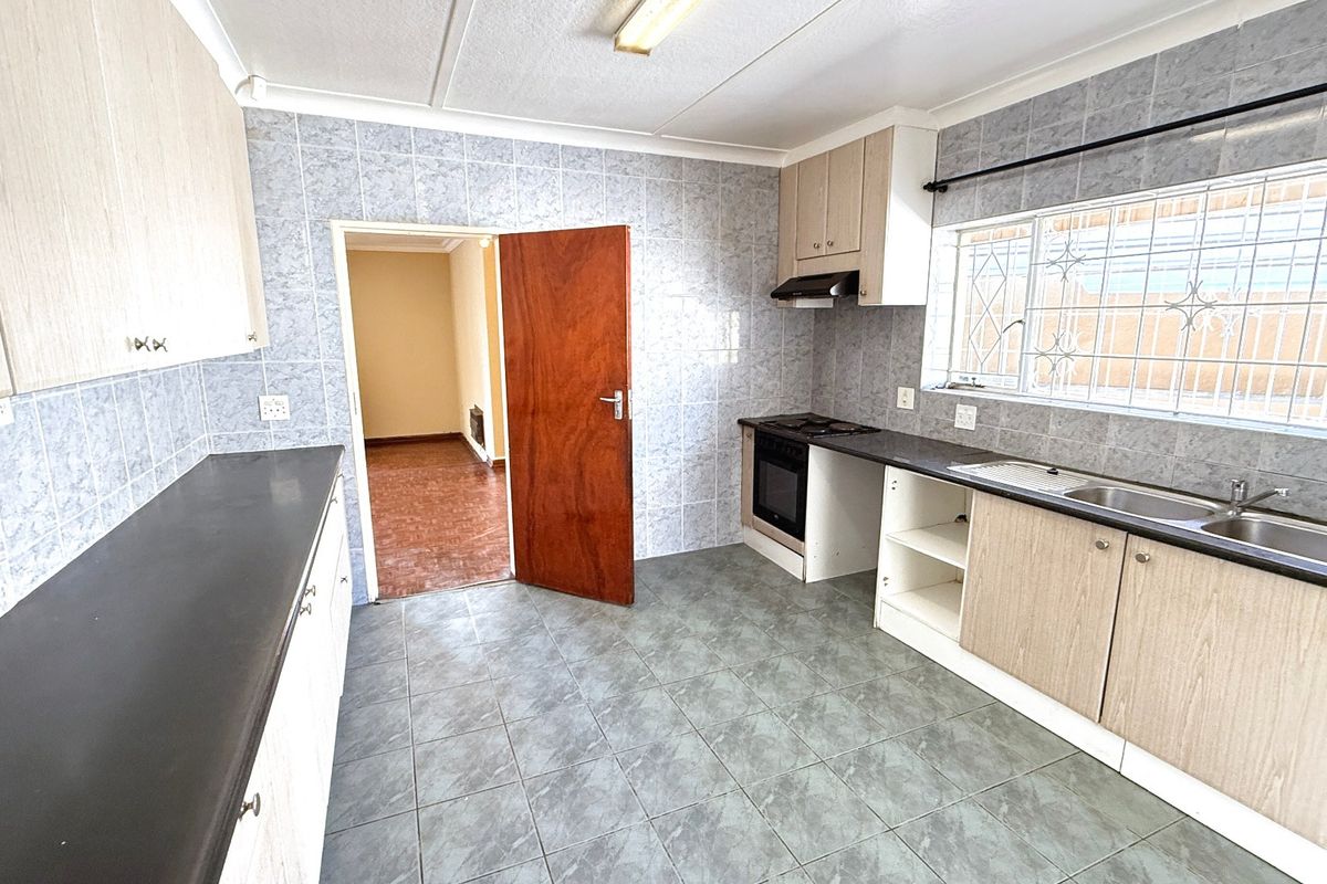 A functional kitchen featuring tiled walls and floors, built-in cabinetry, an oven with extractor fan, and a stainless steel sink.
