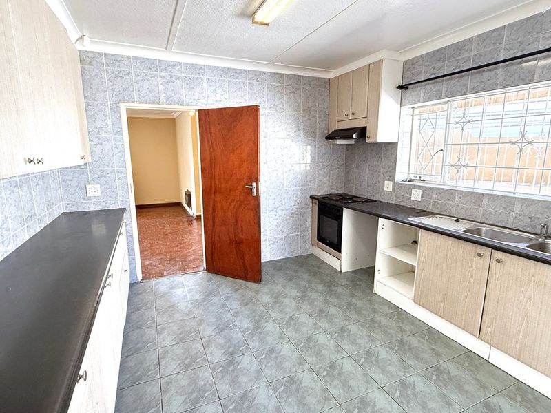 A functional kitchen featuring tiled walls and floors, built-in cabinetry, an oven with extractor fan, and a stainless steel sink.