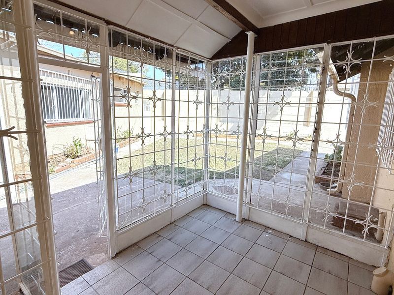 A covered patio area featuring tiled flooring and extensive security gates, overlooking a rear garden space.