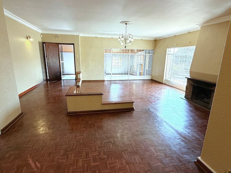 Spacious living room featuring original parquet flooring, a built-in fireplace, and large windows with security gates, offering a versatile open-plan layout.