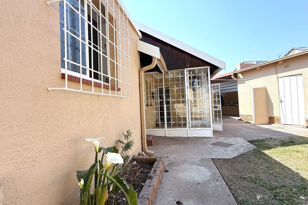 Rear exterior view of the property featuring a concrete pathway, security bars on windows, and a small brick planter area.