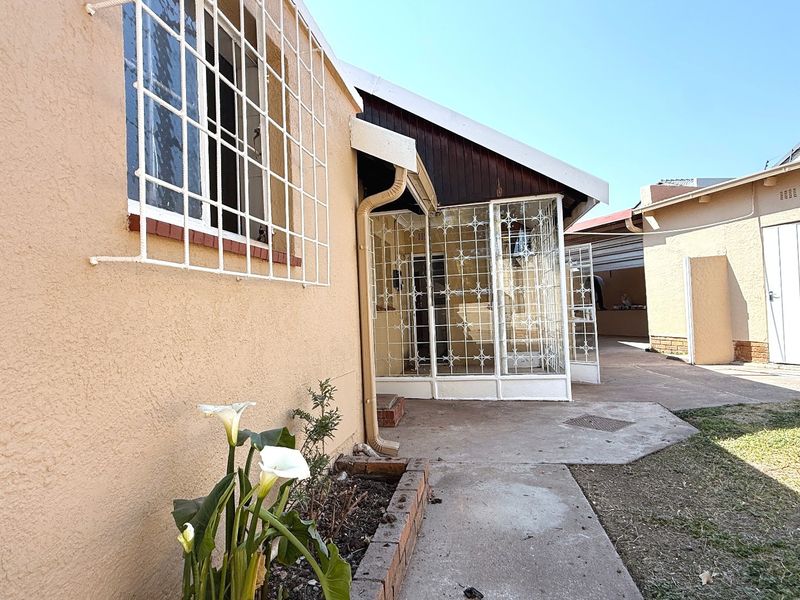 Rear exterior view of the property featuring a concrete pathway, security bars on windows, and a small brick planter area.