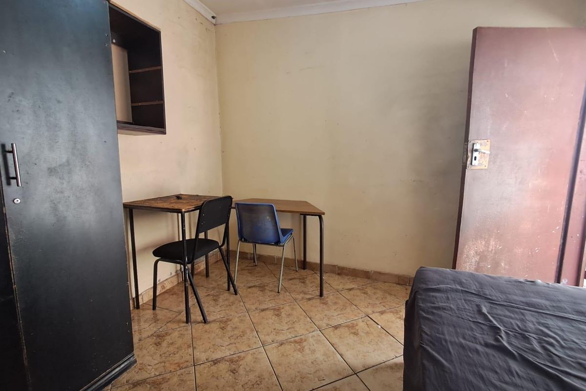 A bedroom featuring tiled flooring and built-in wall shelving, requiring cosmetic updates to the walls and door to improve its overall condition.