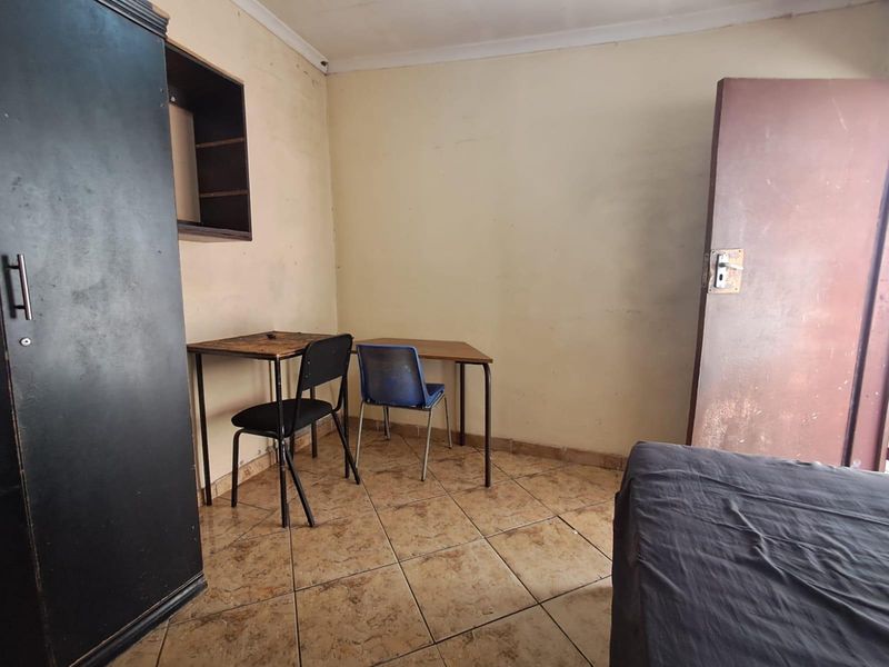 A bedroom featuring tiled flooring and built-in wall shelving, requiring cosmetic updates to the walls and door to improve its overall condition.