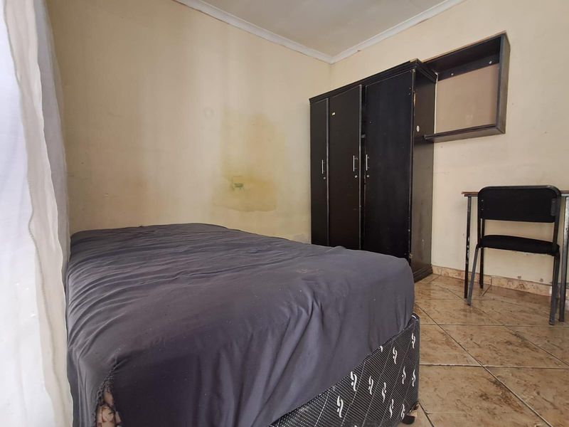 A bedroom featuring tiled flooring and a built-in cupboard, currently requiring cosmetic updates to the wall finishes.
