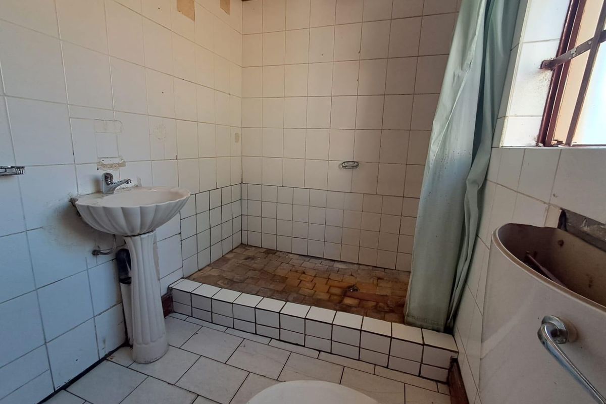 A dated bathroom featuring a pedestal basin, tiled shower area, and toilet, requiring significant renovation and cosmetic updates to restore functionality and appeal.