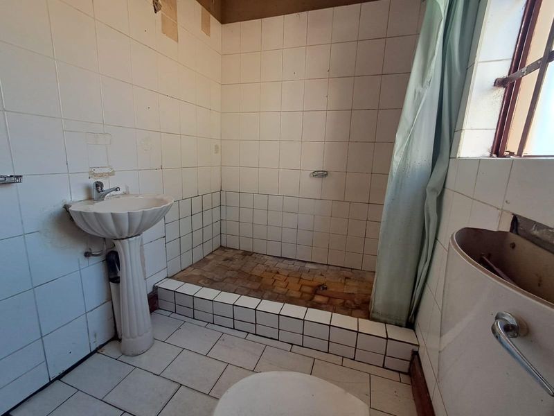 A dated bathroom featuring a pedestal basin, tiled shower area, and toilet, requiring significant renovation and cosmetic updates to restore functionality and appeal.