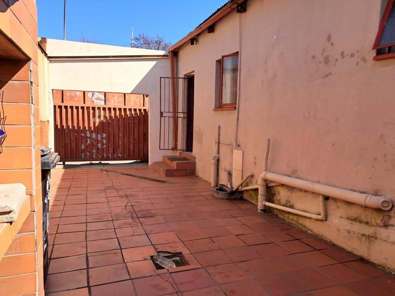 Rear exterior courtyard area featuring tiled flooring, security gate access, and exposed plumbing infrastructure requiring maintenance and repair.