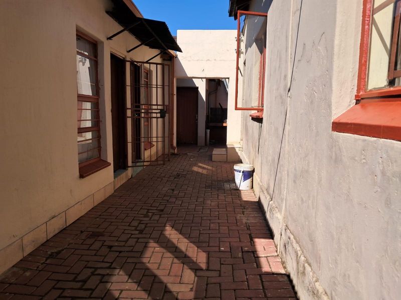 A narrow paved exterior walkway between building sections, featuring security gates and weathered exterior wall finishes.