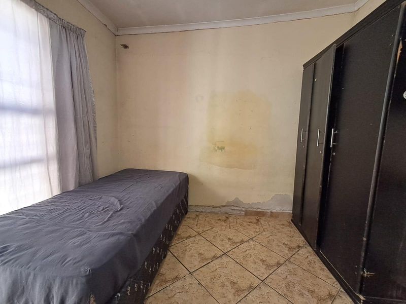 A bedroom featuring tiled flooring and a built-in wardrobe, currently showing signs of wall damage and peeling paint requiring maintenance.