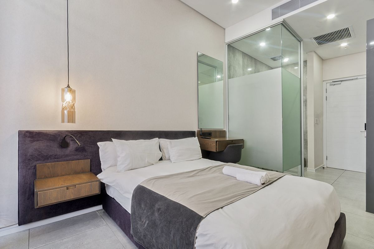 Modern bedroom featuring a built-in headboard, floating bedside table, and a sleek glass-enclosed ensuite bathroom with contemporary finishes.