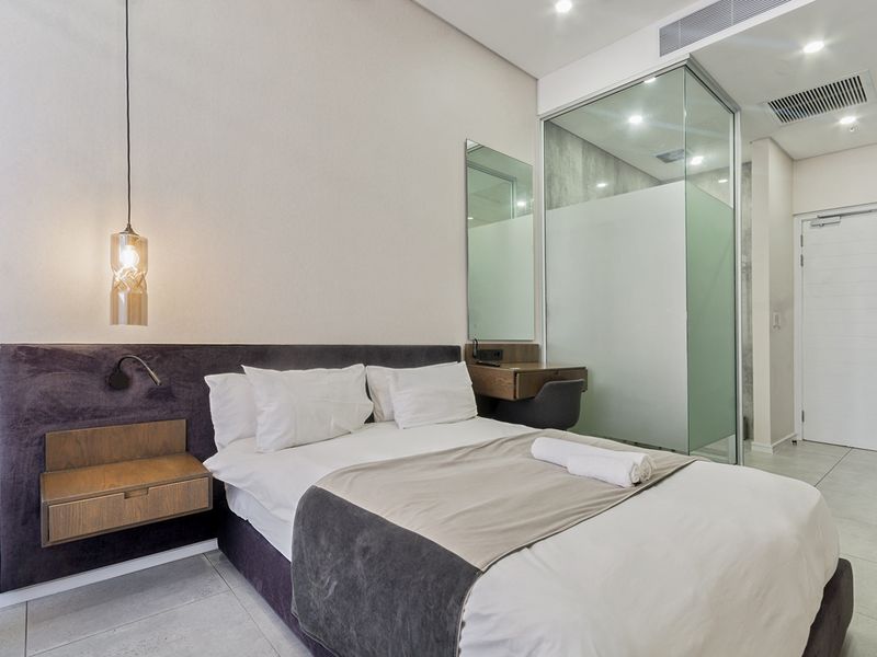 Modern bedroom featuring a built-in headboard, floating bedside table, and a sleek glass-enclosed ensuite bathroom with contemporary finishes.