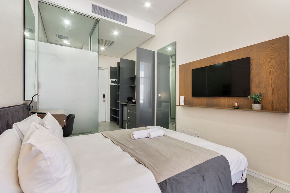 Modern bedroom featuring a glass-enclosed ensuite, built-in cabinetry, wood-paneled feature wall, and recessed lighting in a contemporary apartment setting.